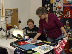 Two quilt makers looking at a T-shirt quilt while it is being sewed.