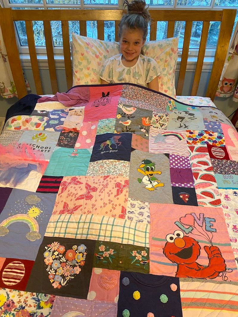 Girl in bed under baby clothes quilt