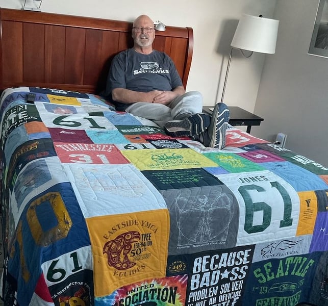 Guy sitting on T-shirt quilt on a bed by Too Cool T-shirt Quilts