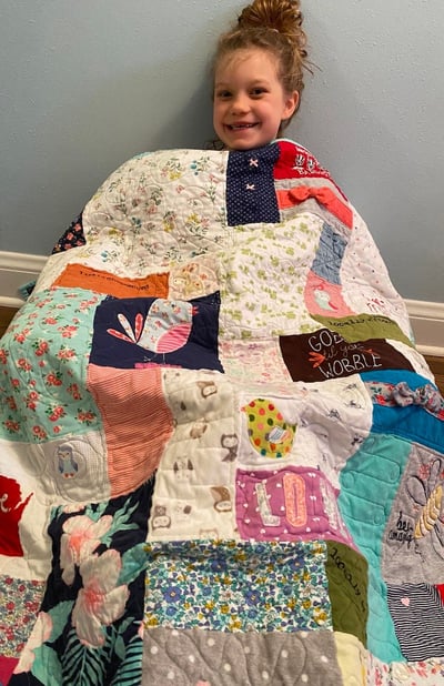 girl sitting on floor under baby clothes quilt